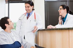 man in wheelchair with broken arms happily talking with doctor and nurses