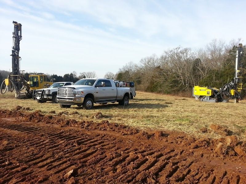 Drilling equipment and trucks in a field with a cloudy sky. Earthmoving equipment on the foreground.