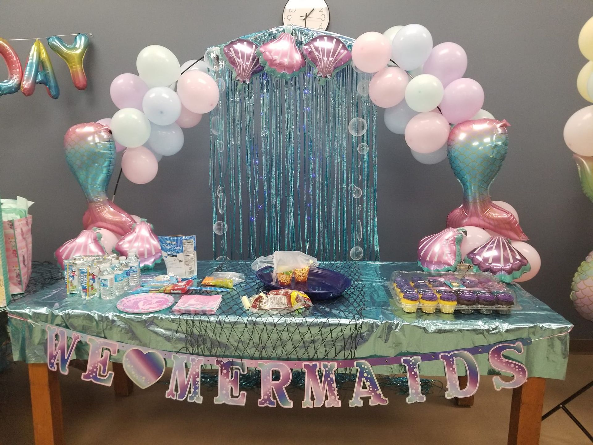A table decorated for a mermaid birthday party with balloons and a banner.