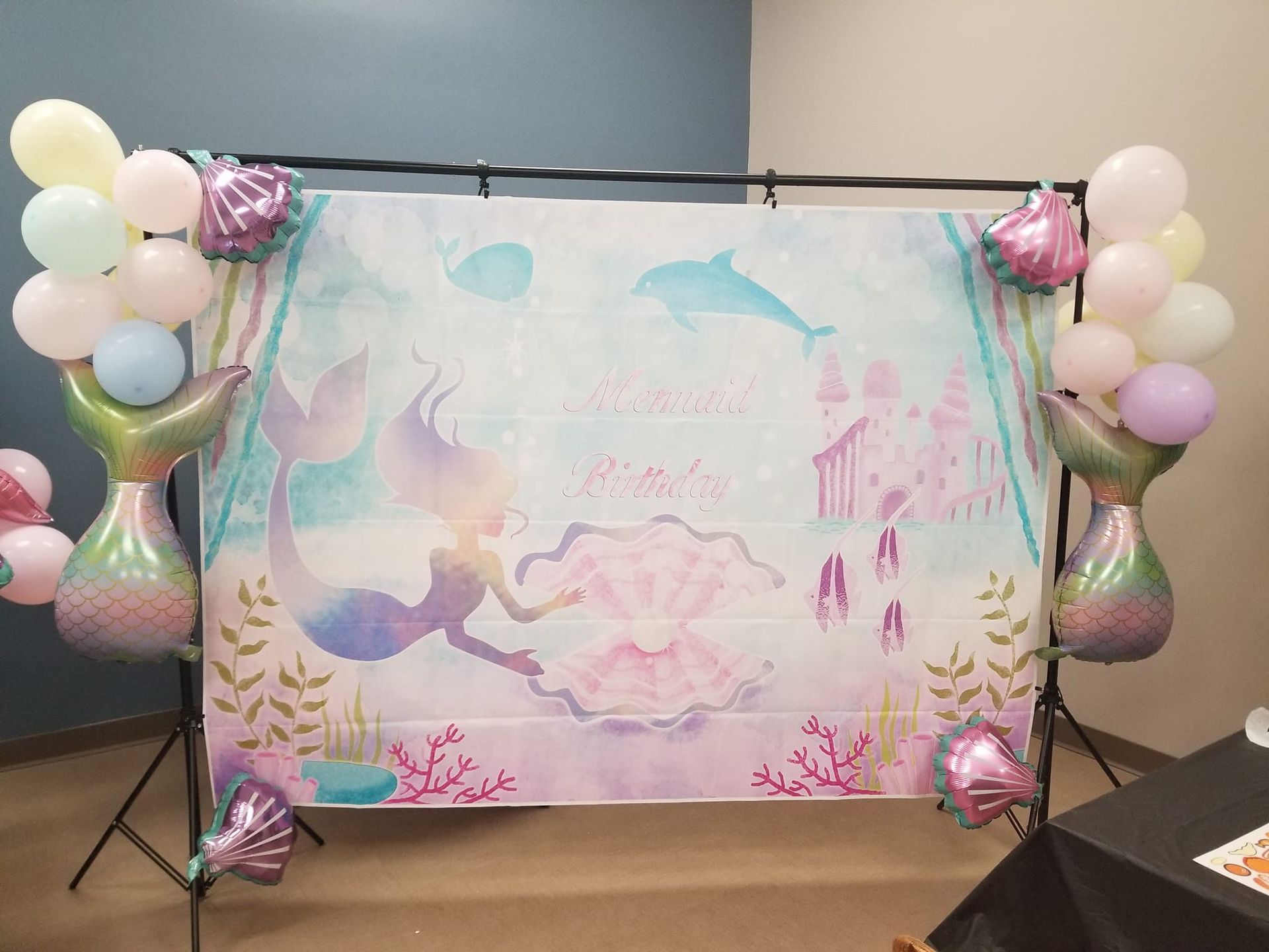 A mermaid birthday backdrop with balloons and a mermaid tail.