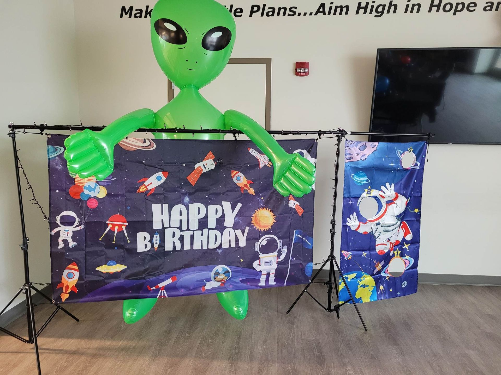 A green alien is holding a happy birthday banner