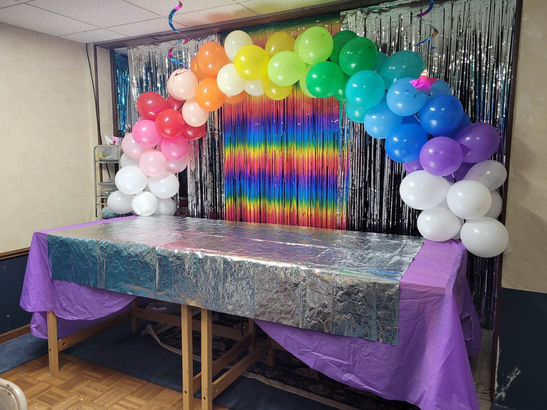 A table is decorated with balloons and a rainbow backdrop.