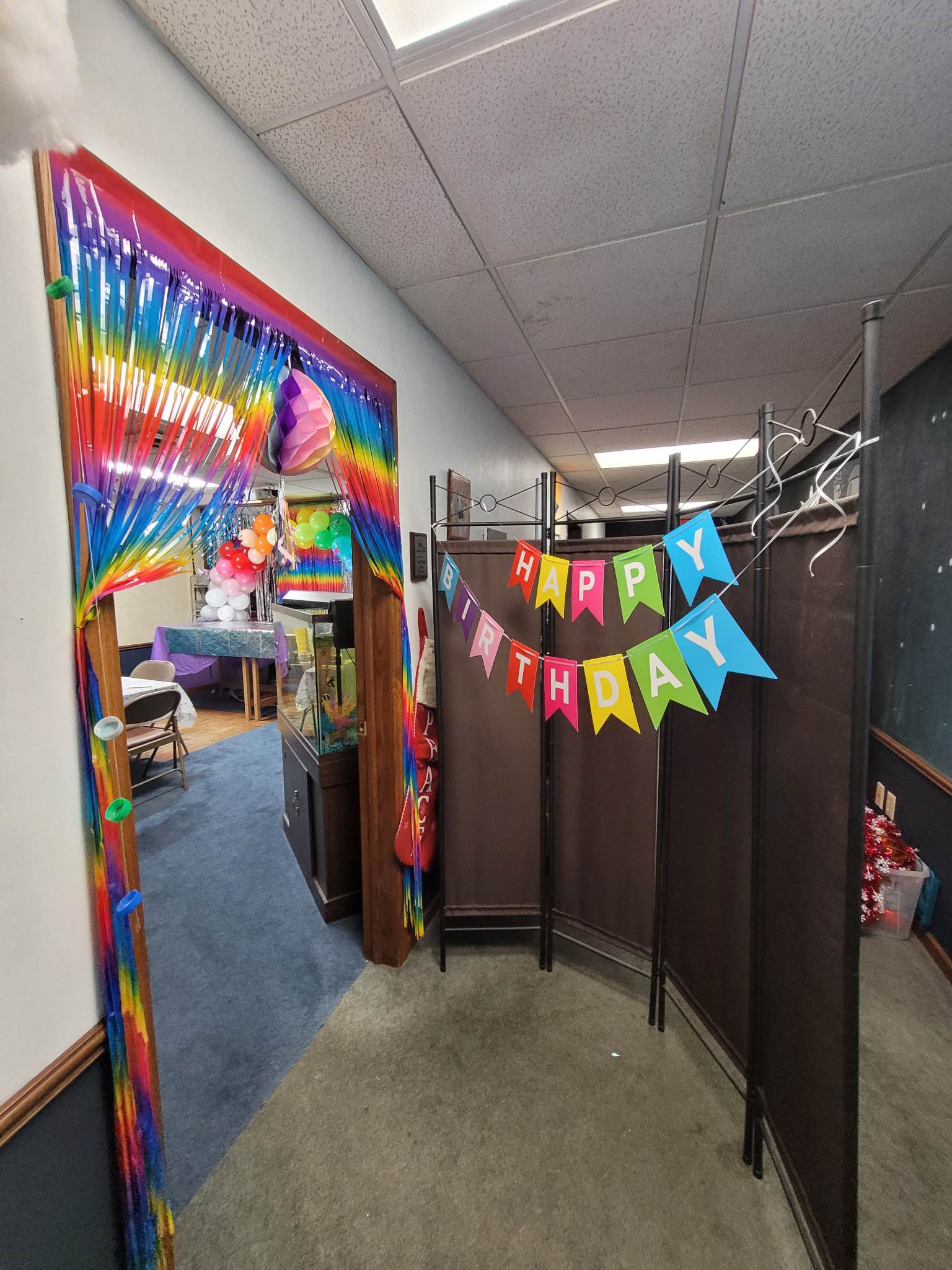 A hallway with a rainbow arch and a happy birthday banner hanging from the ceiling.