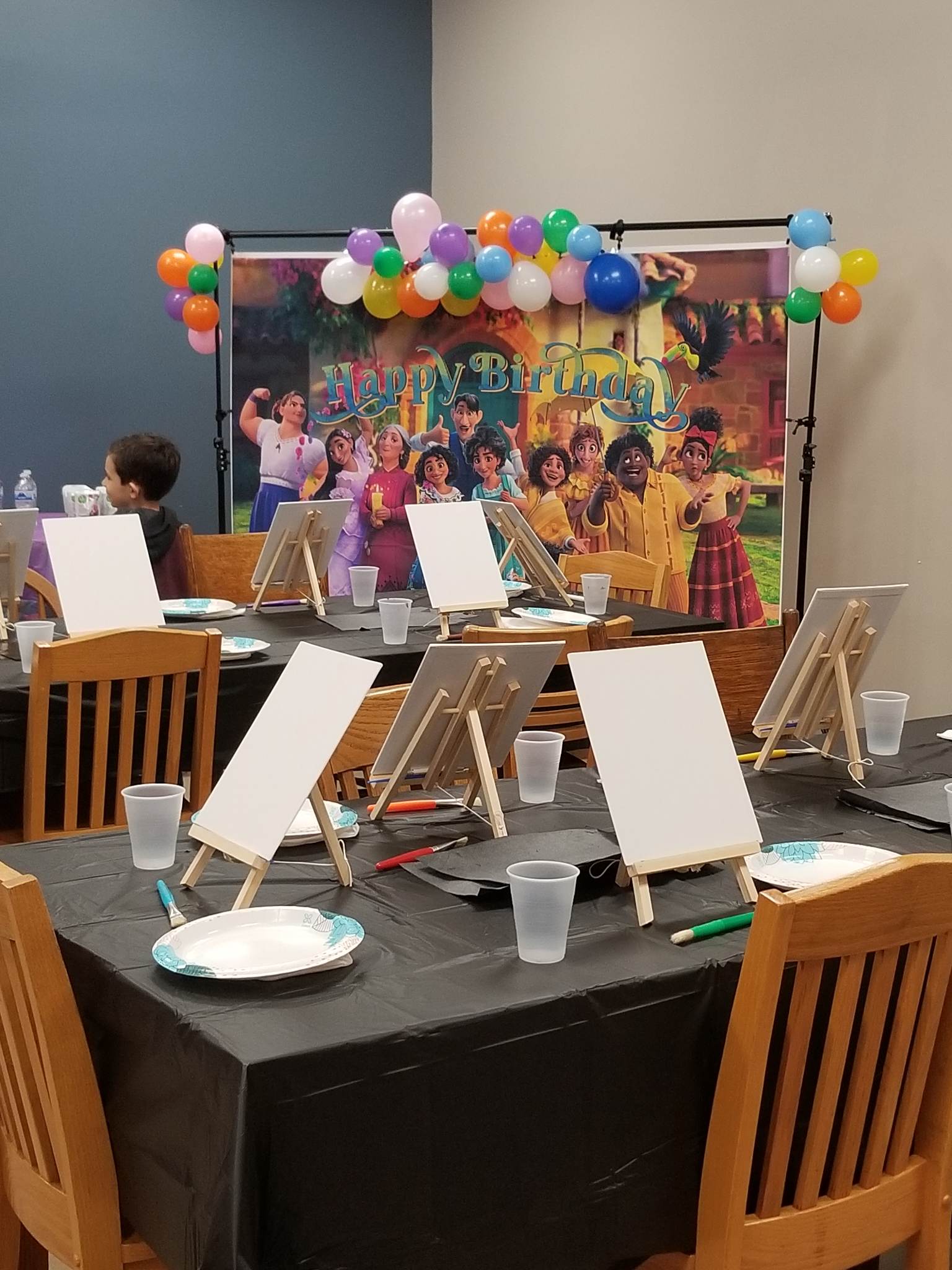 A room filled with tables and chairs with painting easels and balloons.