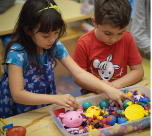 Two children reaching into a bin of colorful small toys and shapes while sitting at a table.