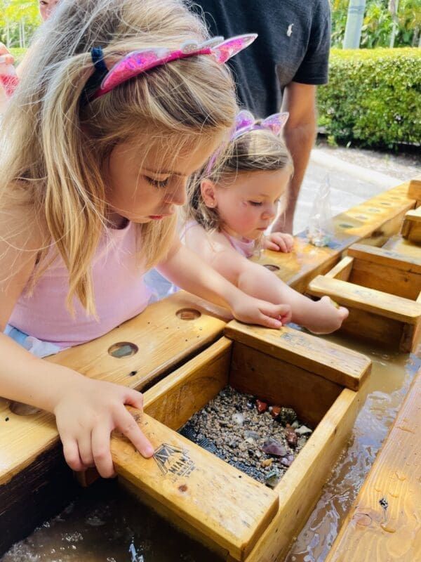 Two little girls are playing with wooden boxes filled with rocks.