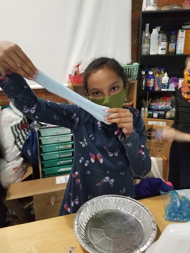 A young girl wearing a mask is playing with slime in a classroom.