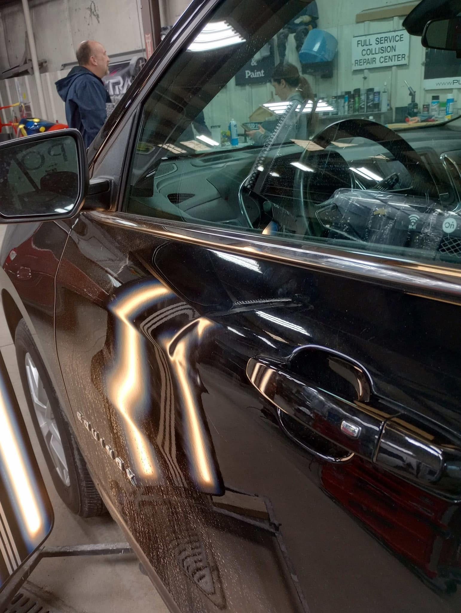 A man is standing next to a black car in a garage.