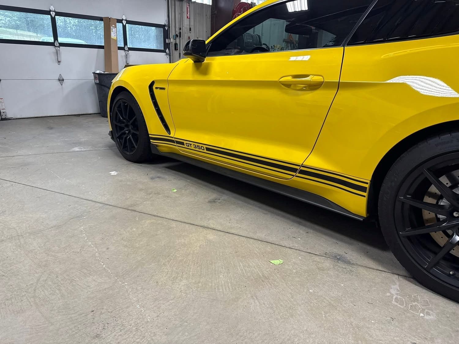 A yellow mustang is parked in a garage next to a garage door.