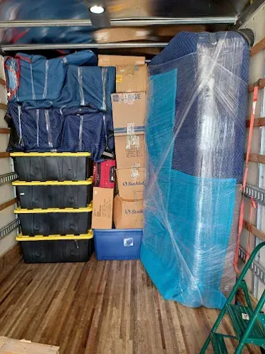 Moving truck loaded with boxes, bins, and furniture wrapped in plastic, ready for transport.