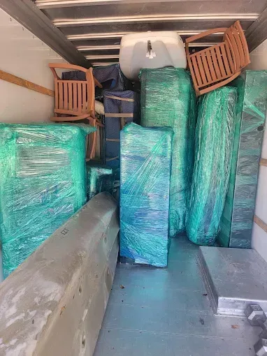 Packed moving truck with furniture wrapped in green plastic and a few chairs stacked at the front
