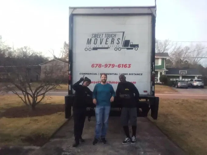 Three people pose in front of a Sweet Peach Movers truck. Two on sides, one in the center, all smiling.