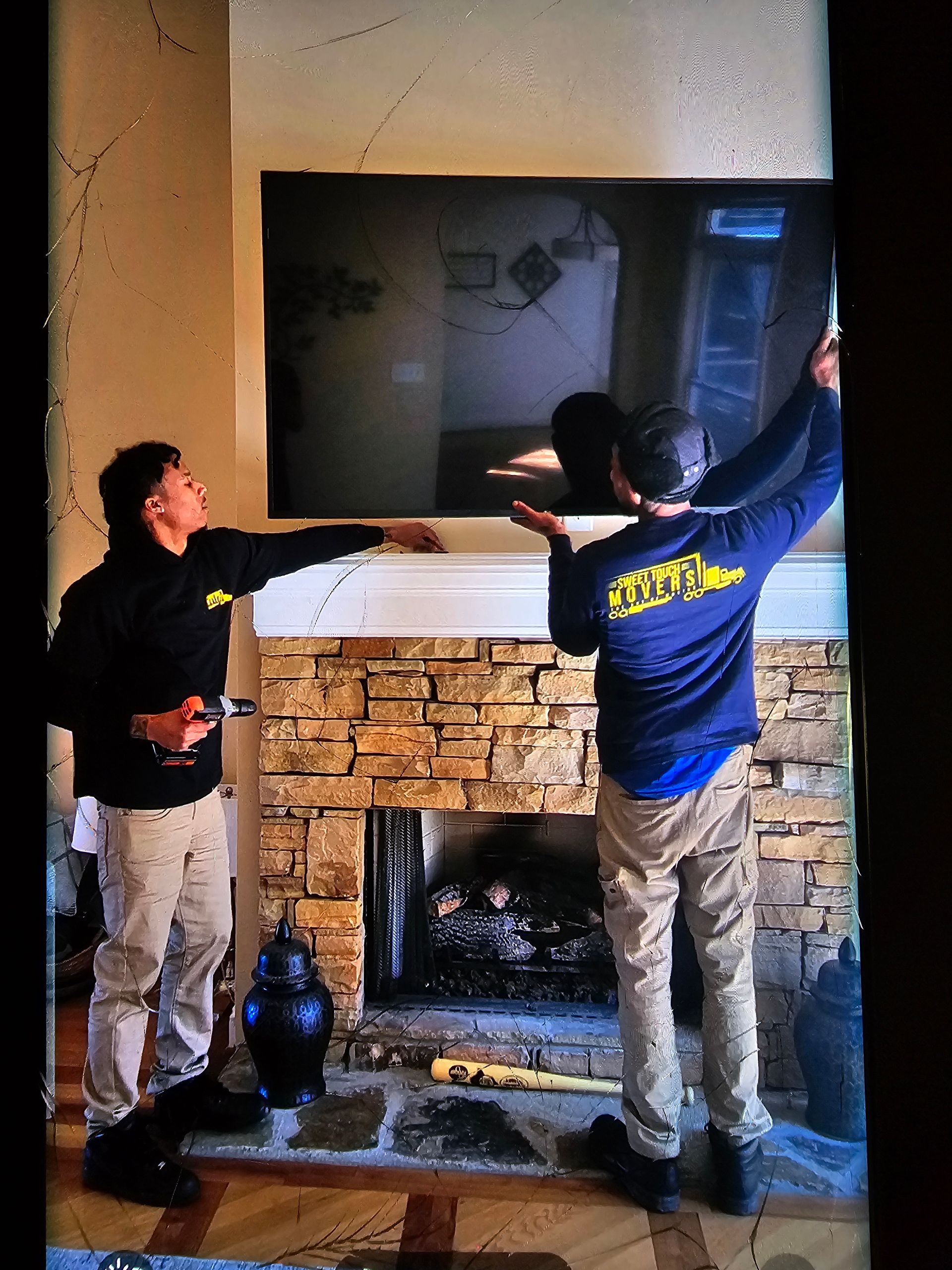 Two men installing a large screen above a stone fireplace. One man points while the other holds up the screen.
