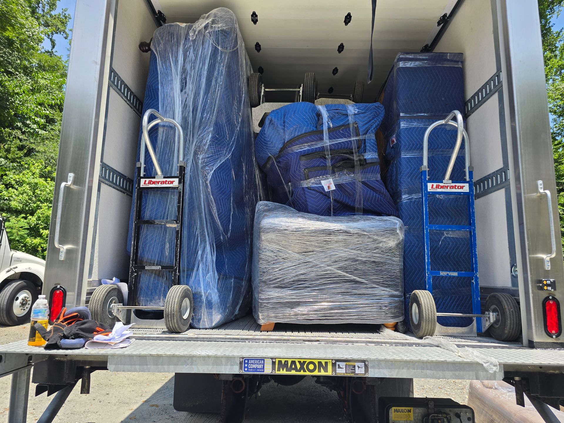 The inside of a moving truck is packed with wrapped furniture and boxes. Two hand trucks stand on either side.