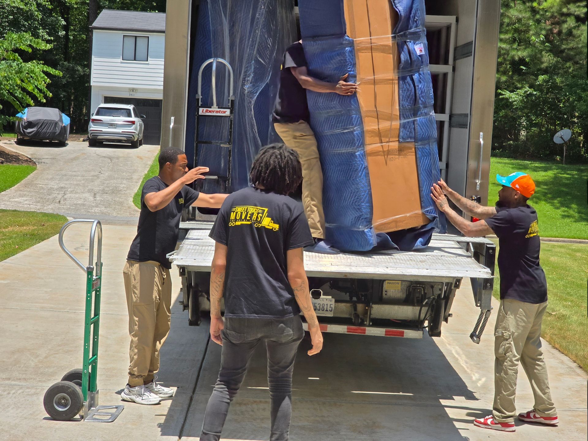 Moving crew loading furniture into a truck on a sunny day. Four people are working together, with one holding a hand truck.
