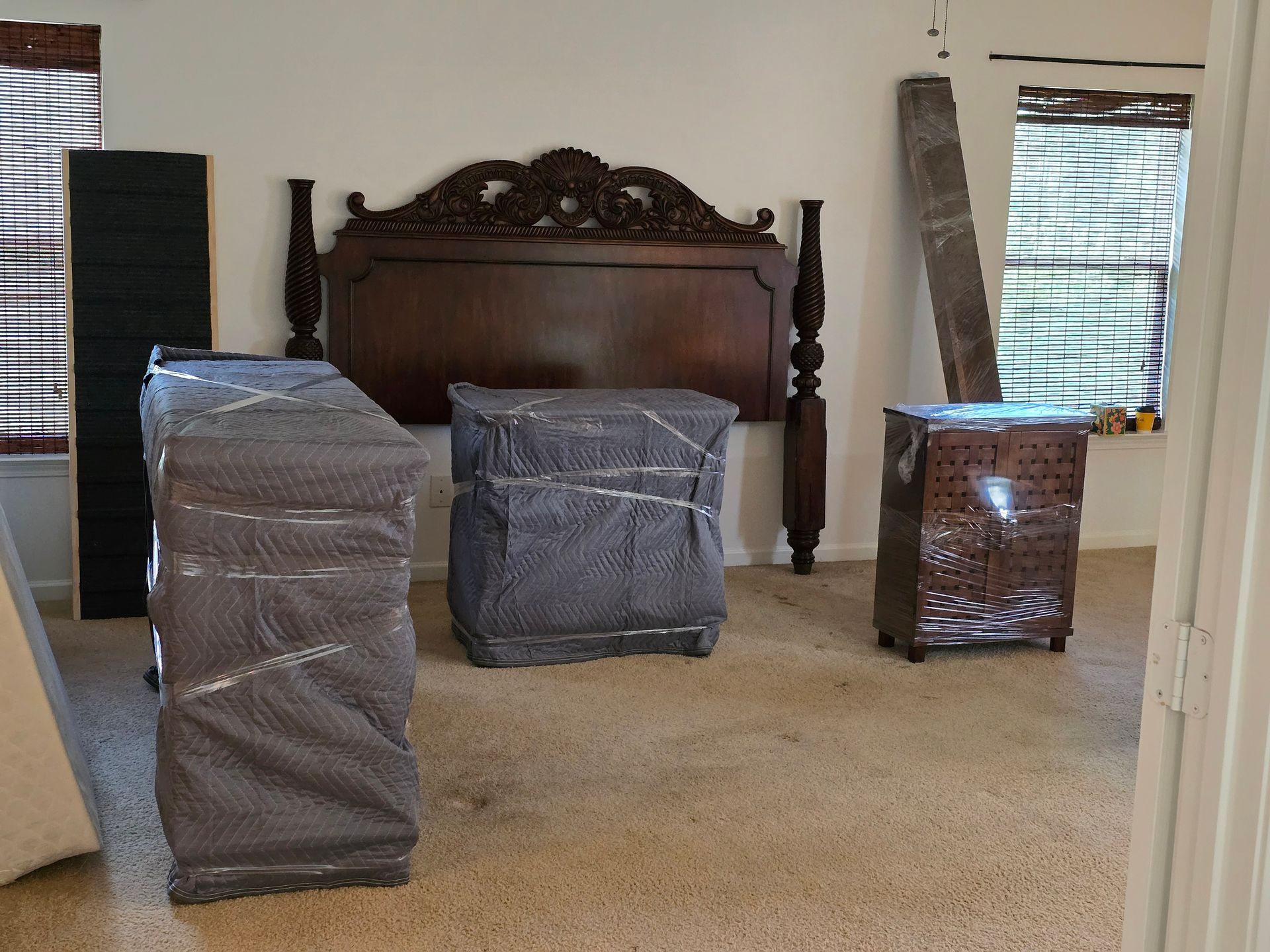 Mover unfolding a wrapped mattress in a bedroom with several other mattresses nearby