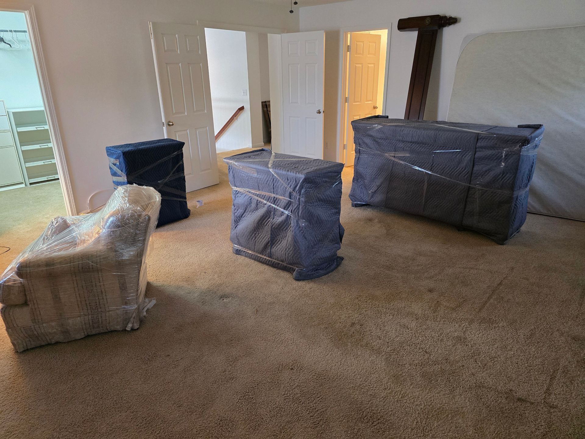 Furniture wrapped in protective covers inside a room with carpet, doors, and a built-in closet.