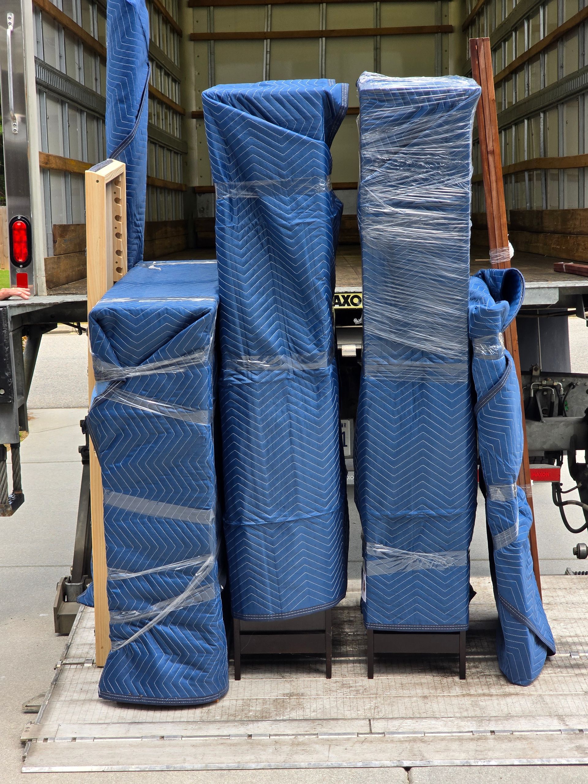 Furniture wrapped in blue moving blankets and plastic wrap inside a truck, ready for transport.