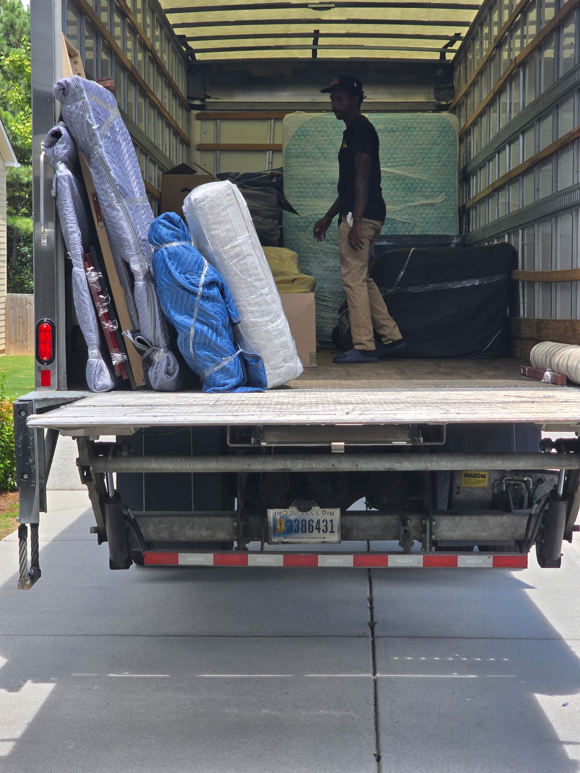 Two movers unloading a packed moving truck. Items include furniture and rolled rugs. One worker is walking inside the truck.
