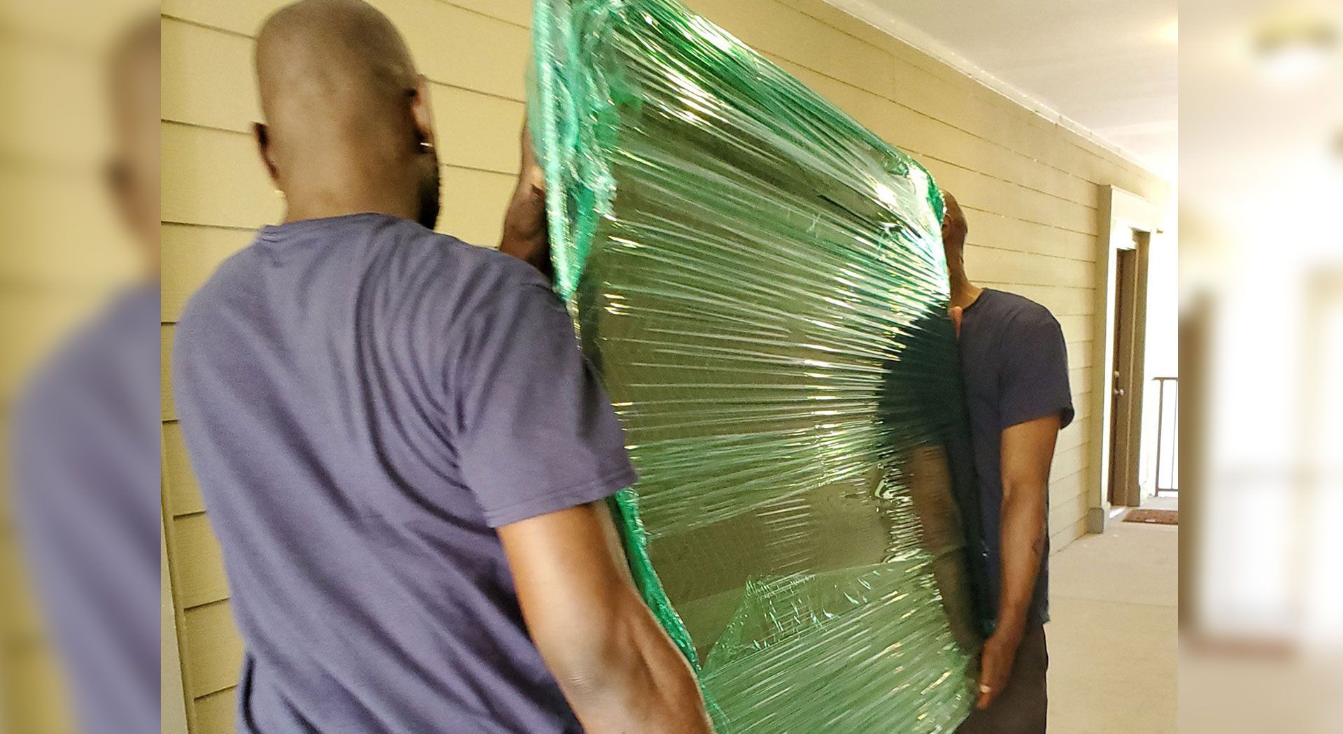 Two people carrying a large, plastic-wrapped mattress through a hallway