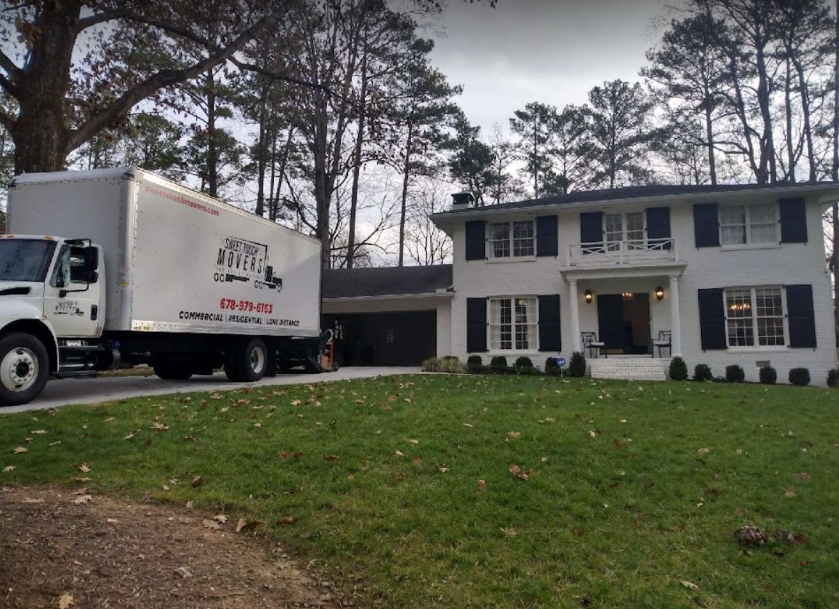 A white moving truck is parked in front of a white house.