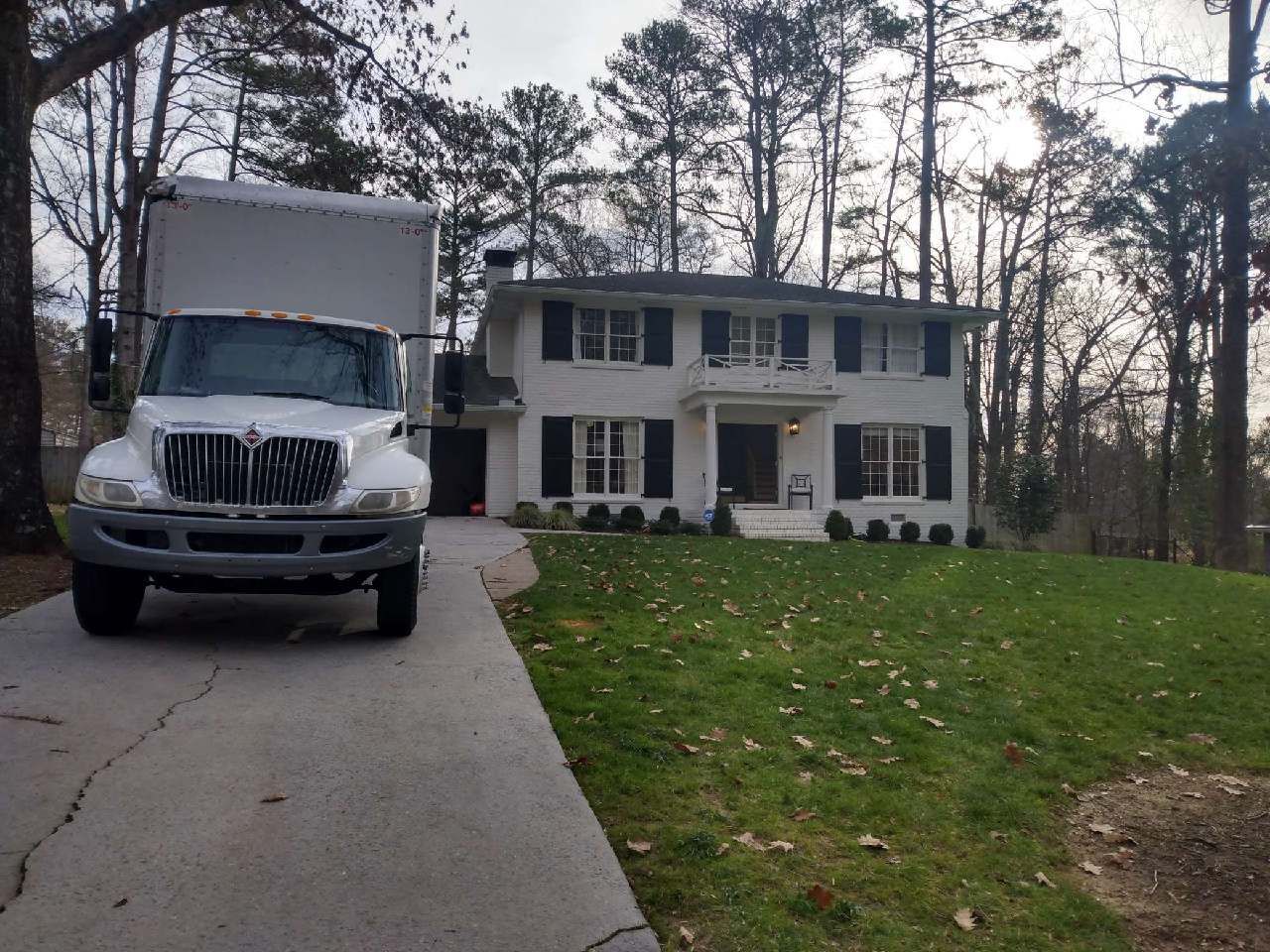A white moving truck is parked in front of a large white house