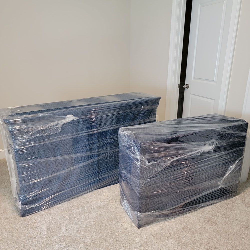 Two blue plastic-wrapped dressers in a carpeted room beside a white door.