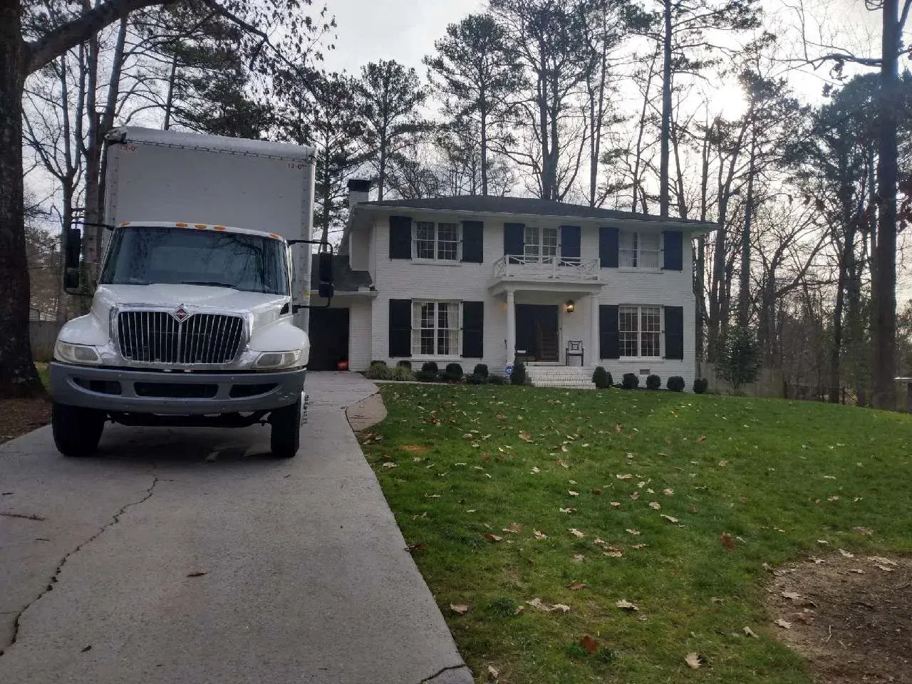 Moving truck parked in front of a two-story white house with black shutters.