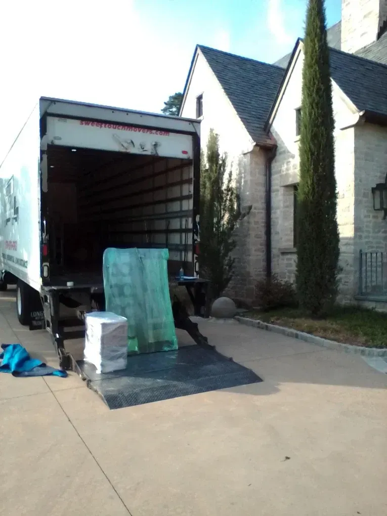 Moving truck backed up to a house; ramp down, items wrapped in protective materials.