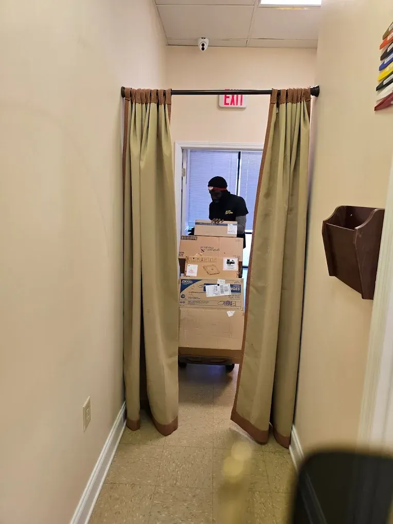 Person moving boxes on a dolly through a doorway with beige curtains. Beige walls and white trim.