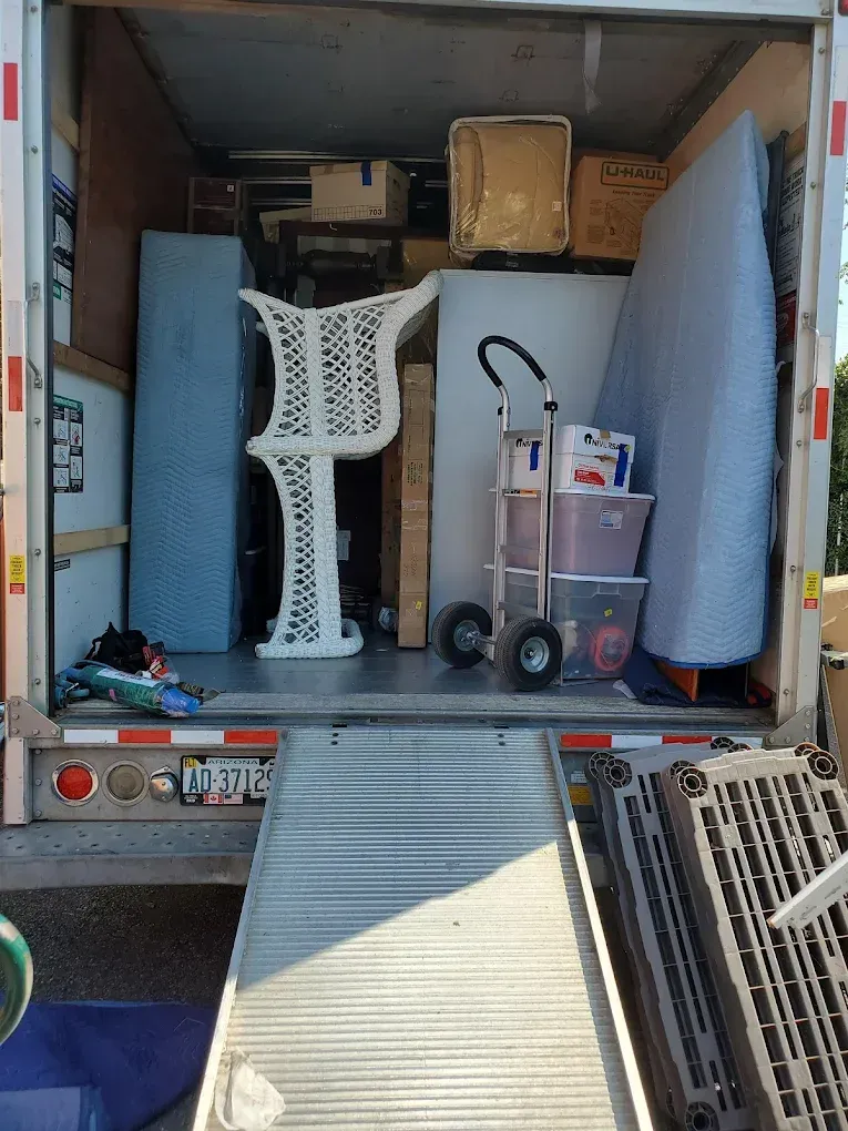 A truck bed loaded with furniture and boxes, including a white decorative table and a mattress, ready for transport.