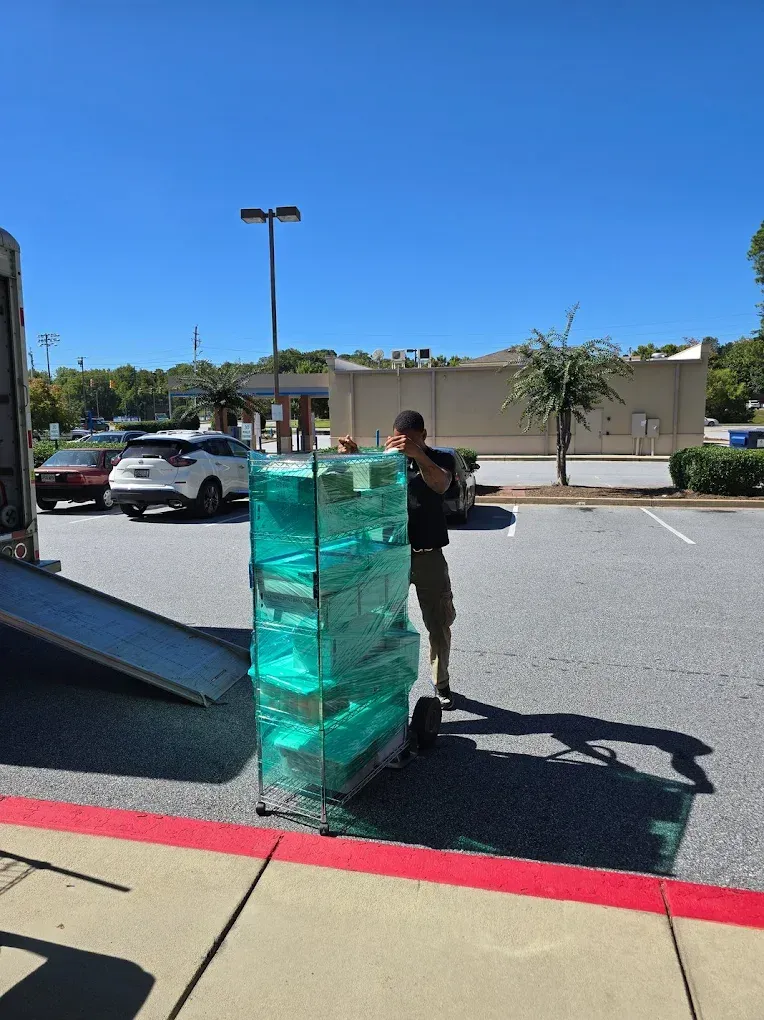 Person loading stack of teal plastic containers onto truck in parking lot.