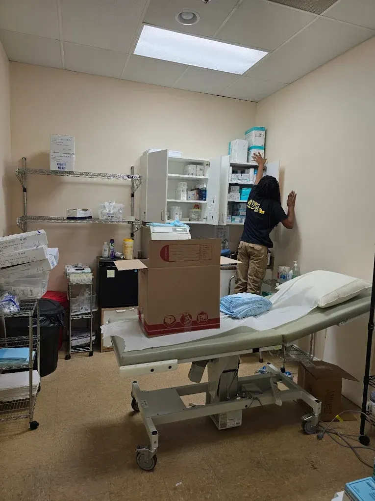 Person reaching, putting something on a wall in a medical room with an examination table and supplies.