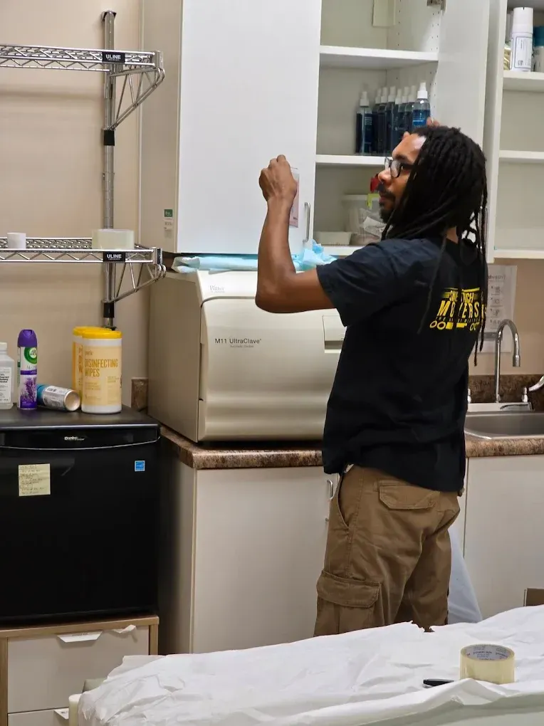 Man in black shirt reaching into cabinet above medical sterilizer in a medical office.