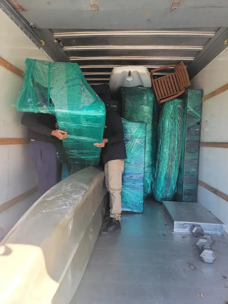 Two people loading wrapped furniture into a truck.