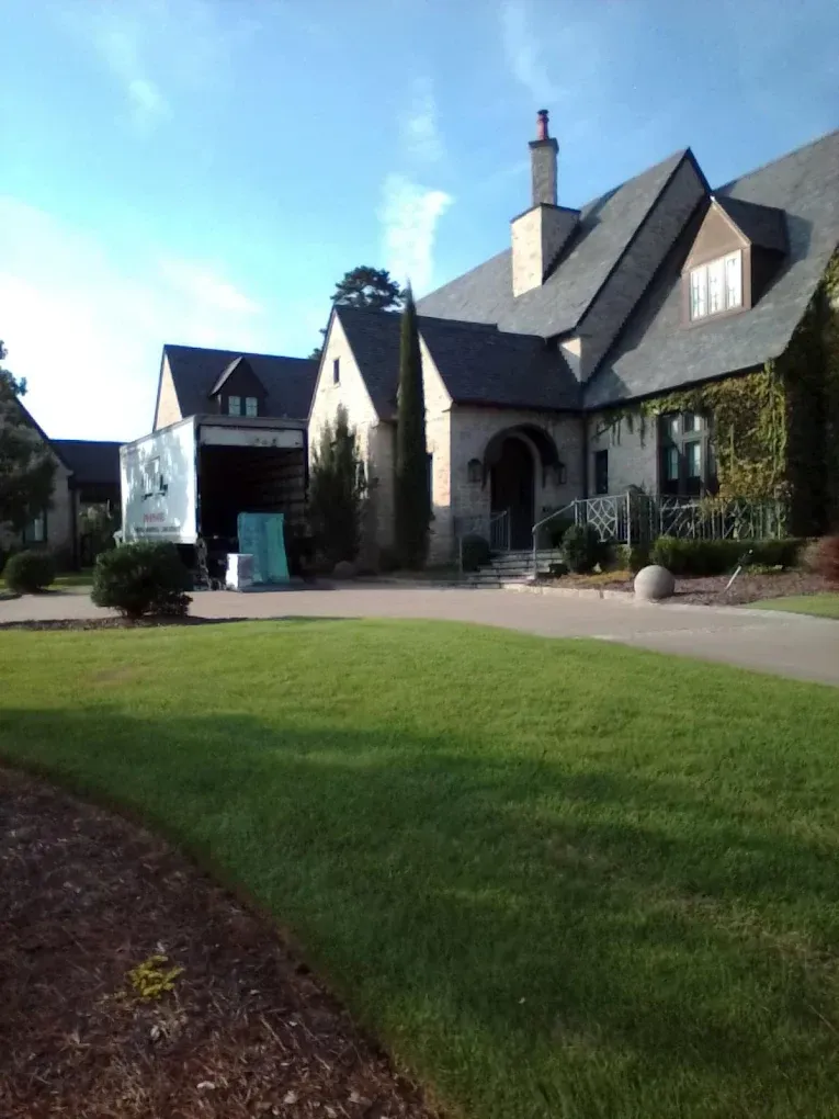 A large stone house with a dark roof and ivy, with a delivery truck parked in the driveway.