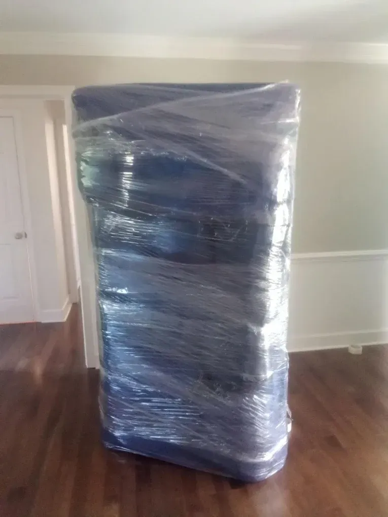 Blue upholstered furniture wrapped in clear plastic on a hardwood floor.