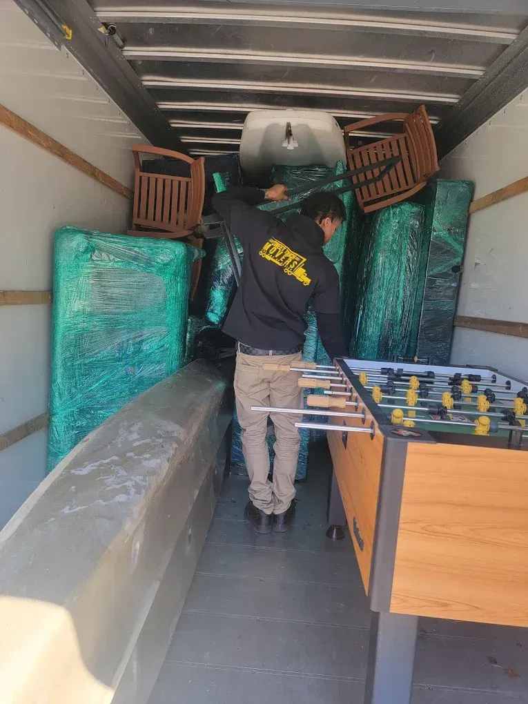Man loading moving truck, surrounded by furniture wrapped in green plastic.