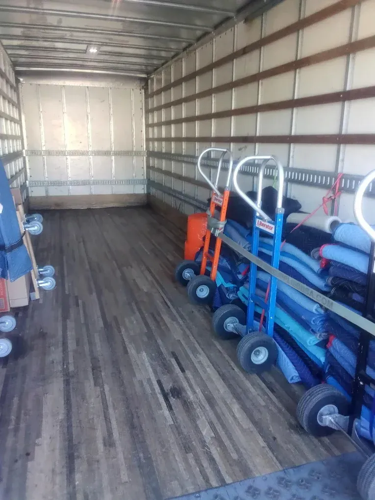 Interior of a moving truck with hand trucks and rolled-up rugs.