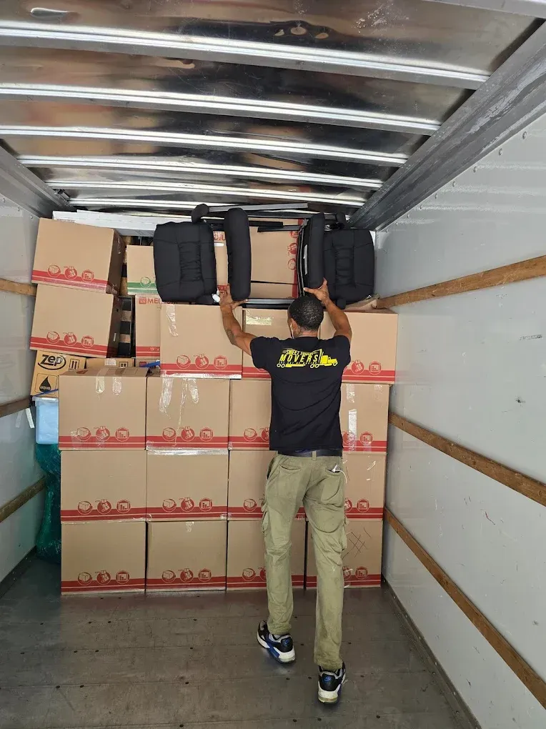 Man inside a moving truck, placing two black seats above boxes.