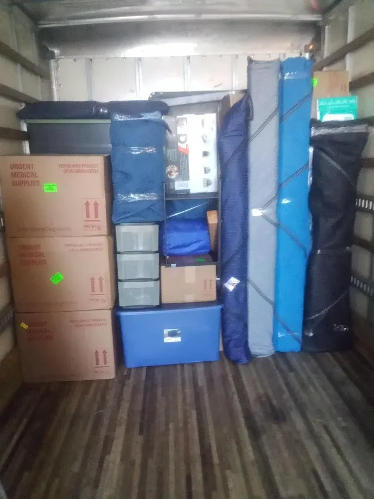 A moving truck interior filled with boxes, wrapped items, and long, cylindrical bags.