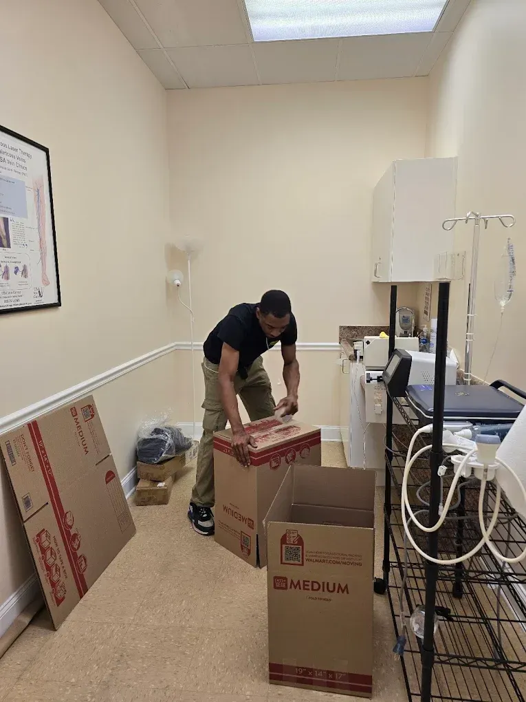 Man unpacking boxes in a room with medical equipment, possibly moving or setting up.