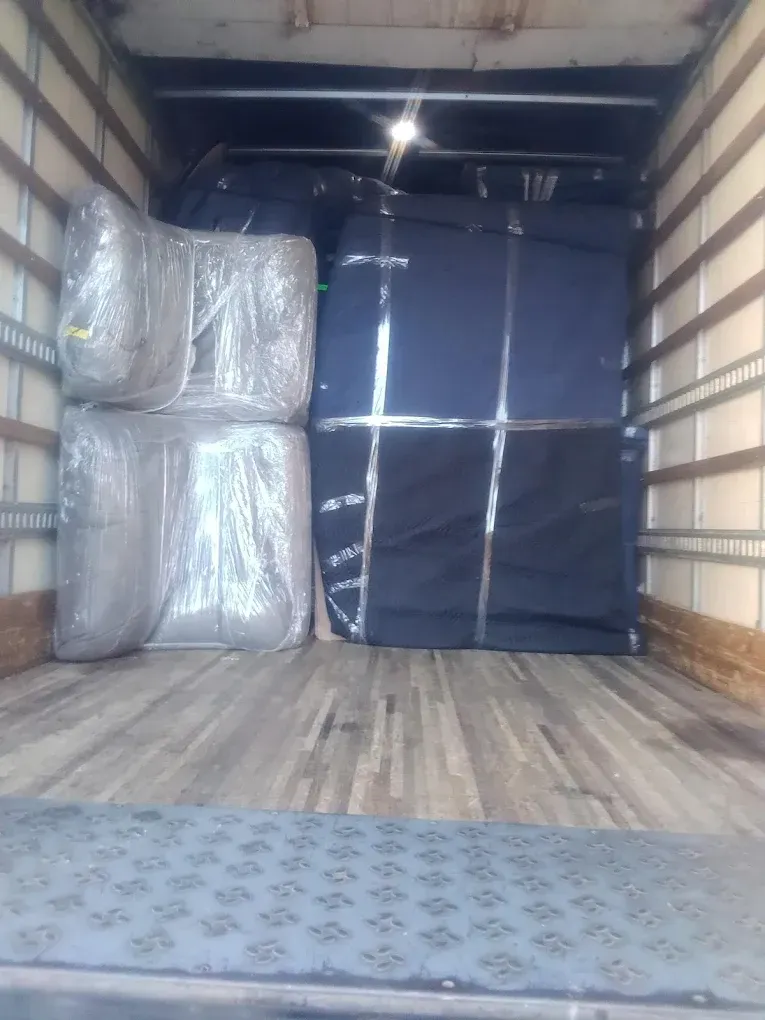 Truck bed filled with wrapped furniture: mattresses and other items.