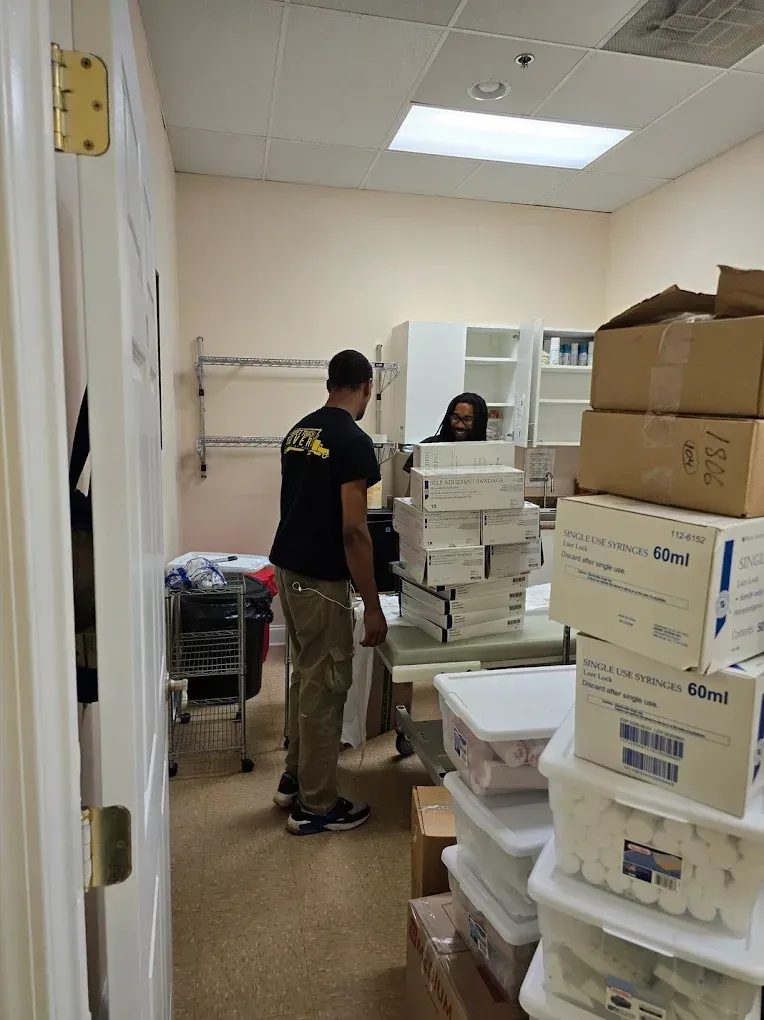 Two people in a small room with stacked boxes, a table, and shelves.
