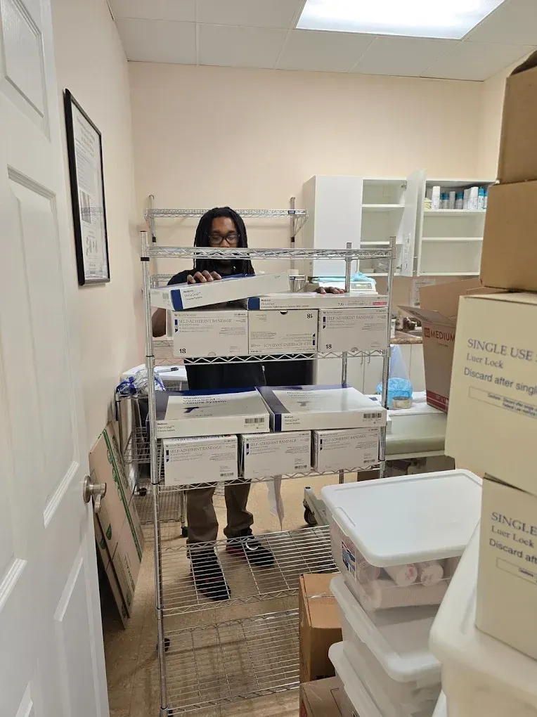 Person standing behind metal shelves filled with boxes in a cluttered room.