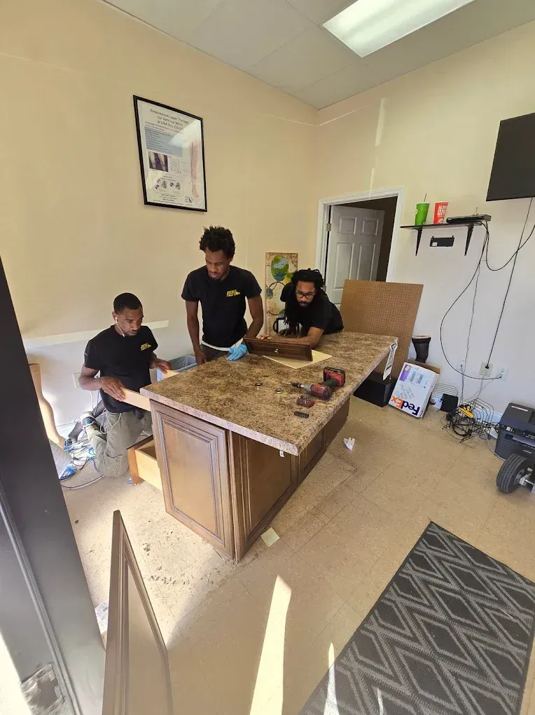Three people installing a kitchen island in a room. Tools are visible on the countertop.