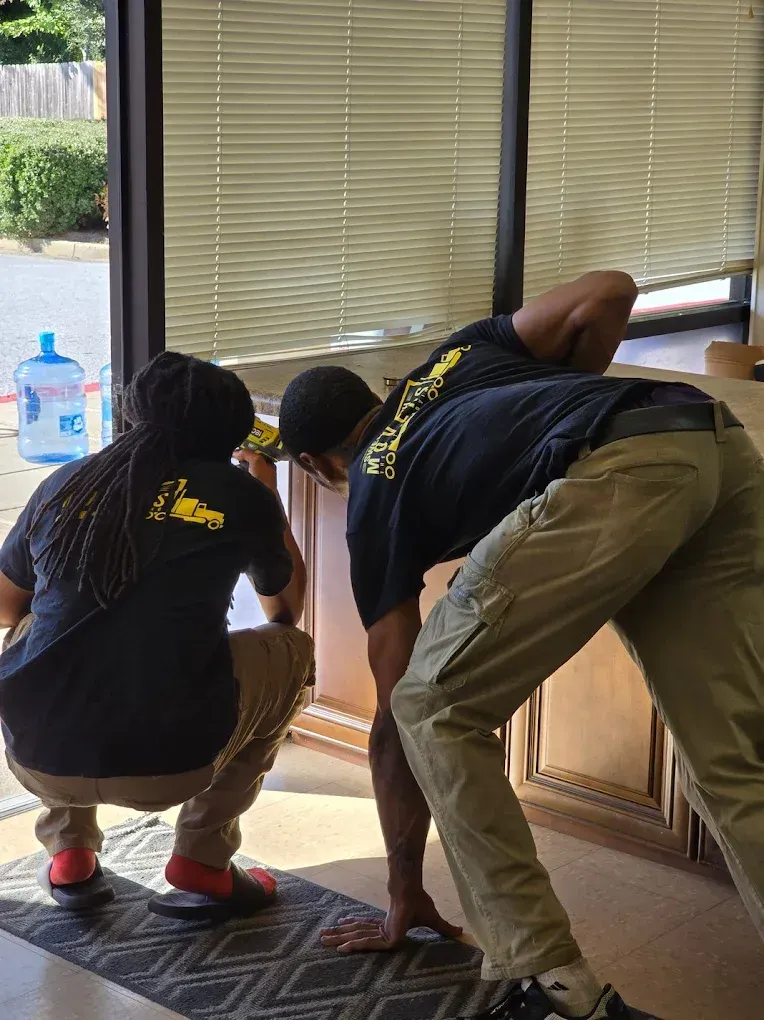 Two people in black shirts and khaki pants, installing something inside a building.