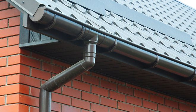 Black rain gutter and downspout on a brick house roof edge