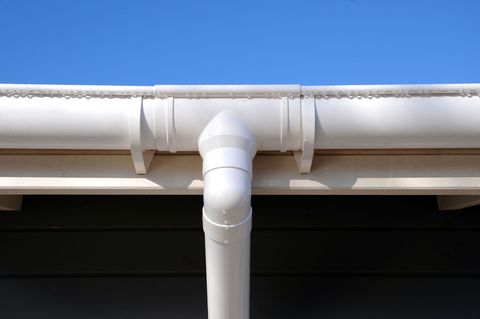 White PVC downspout connected to a gutter against a blue sky and roofline
