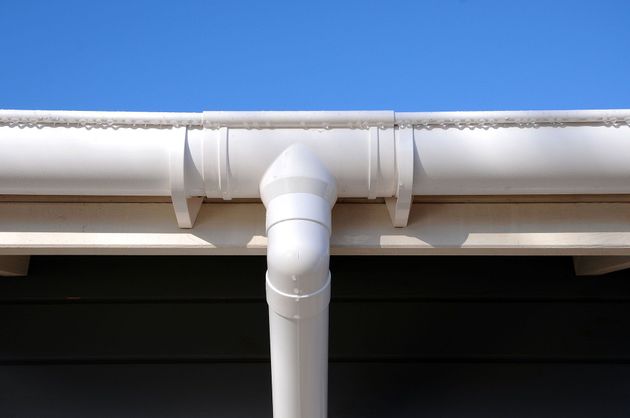 White PVC downspout connected to a gutter against a blue sky and roofline